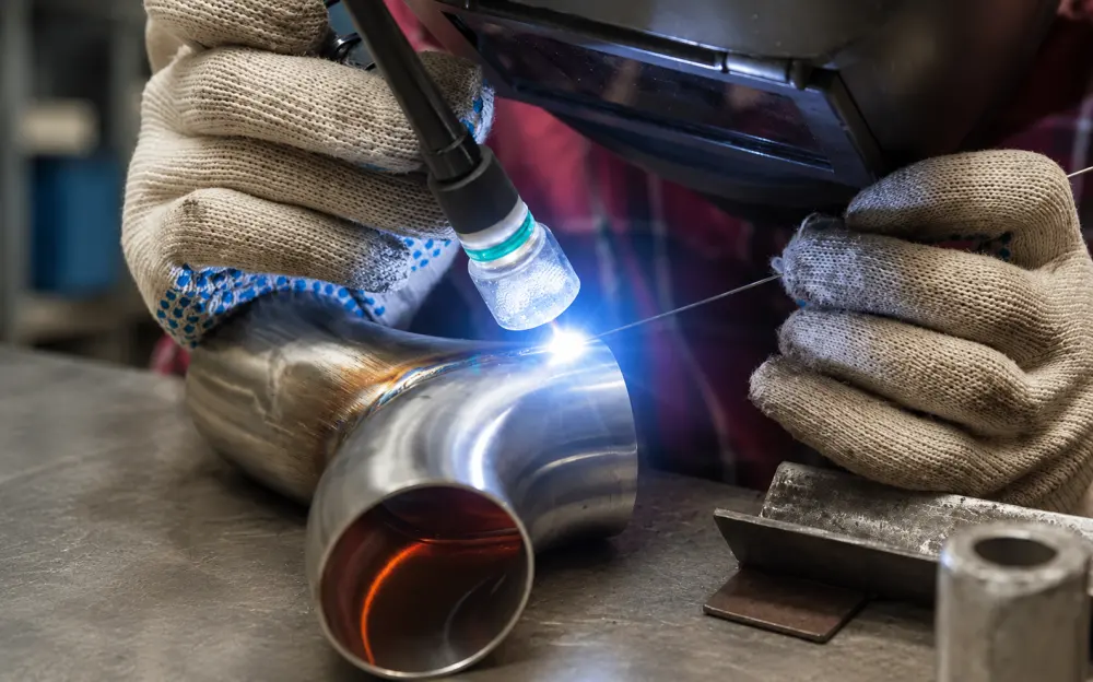 Worker performing argon arc welding on a stainless steel pipe fitting